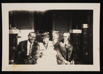 Older woman holding a baby, seated between two unidentified men